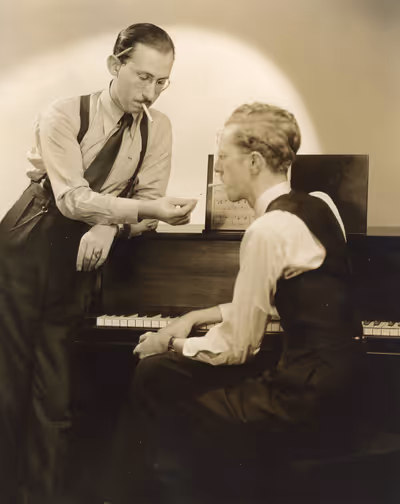 Sammy Cahn and Saul Chaplin with a piano and smoking cigarettes.